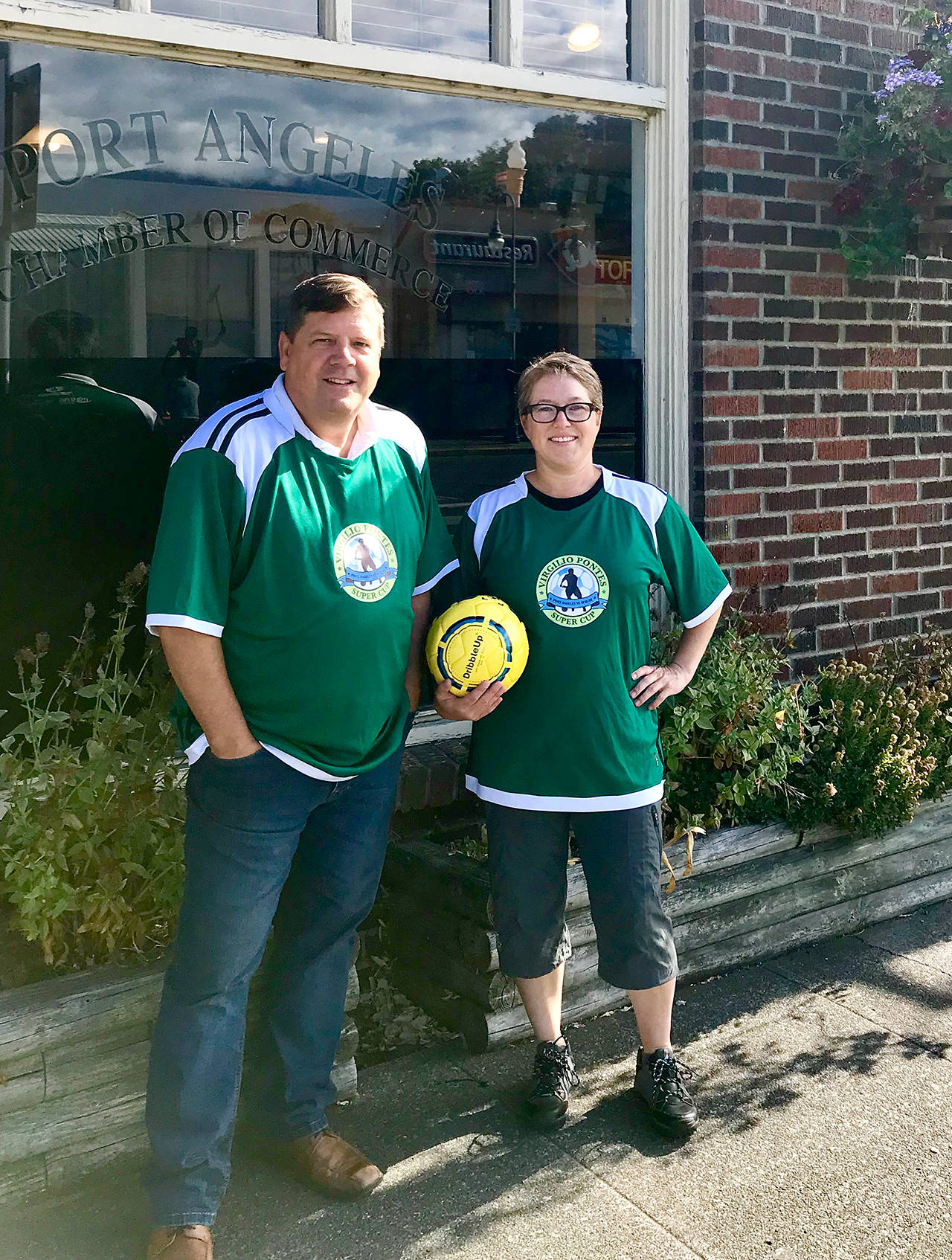 Port Angeles Regional Chamber of Commerce executive director Marc Abshire and city of Port Angeles Deputy Mayor Kate Dexter model the uniforms Port Angeles men’s and women’s teams will wear in Saturday’s Super Cup derby against Sequim at Civic Field. The women’s game kicks off at 5 p.m. with the men following at 7 p.m. Abshire and Dexter have friendly bets on the outcome of the games with Sequim Deputy Mayor Candace Pratt and Sequim Chamber president Shenna Younger.                                Christine Loewe