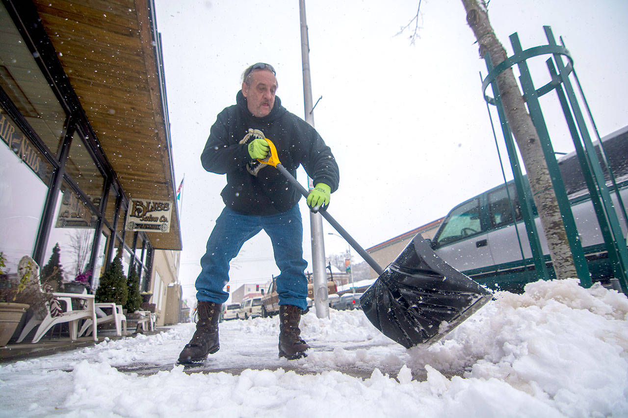 Ron Trouten shovels snow in downtown Port angeles as snow begins to fall Monday afternoon. He said he stopped to clear the sidewalk because “it needs to be done.” (Jesse Major/Peninsula Daily News)