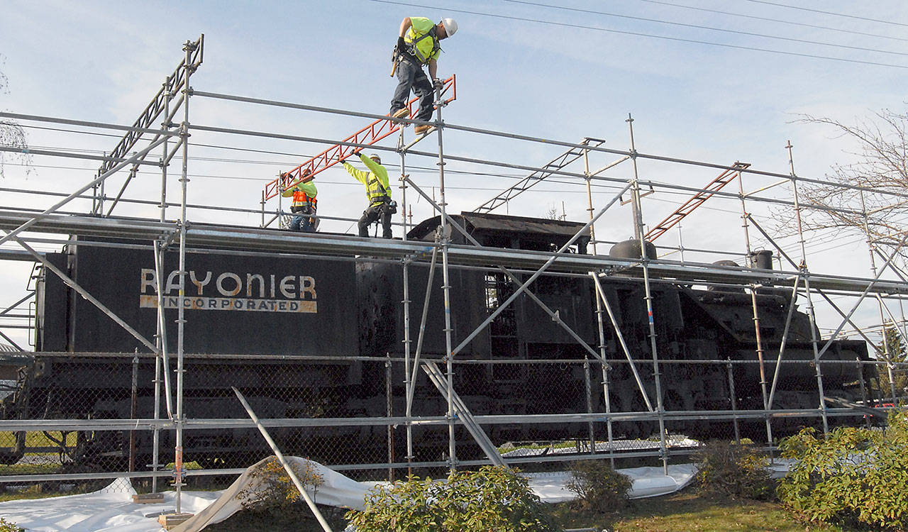 Magnum Construction Services workers, from left, Justin Gans, Alandro Gomez and Jose Duenas erect scaffolding around the Rayonier locomotive on Tuesday at Chase Street and Lauridsen Boulevard in Port Angeles in preparation for asbestos removal from the retired engine. (Keith Thorpe/Peninsula Daily News)