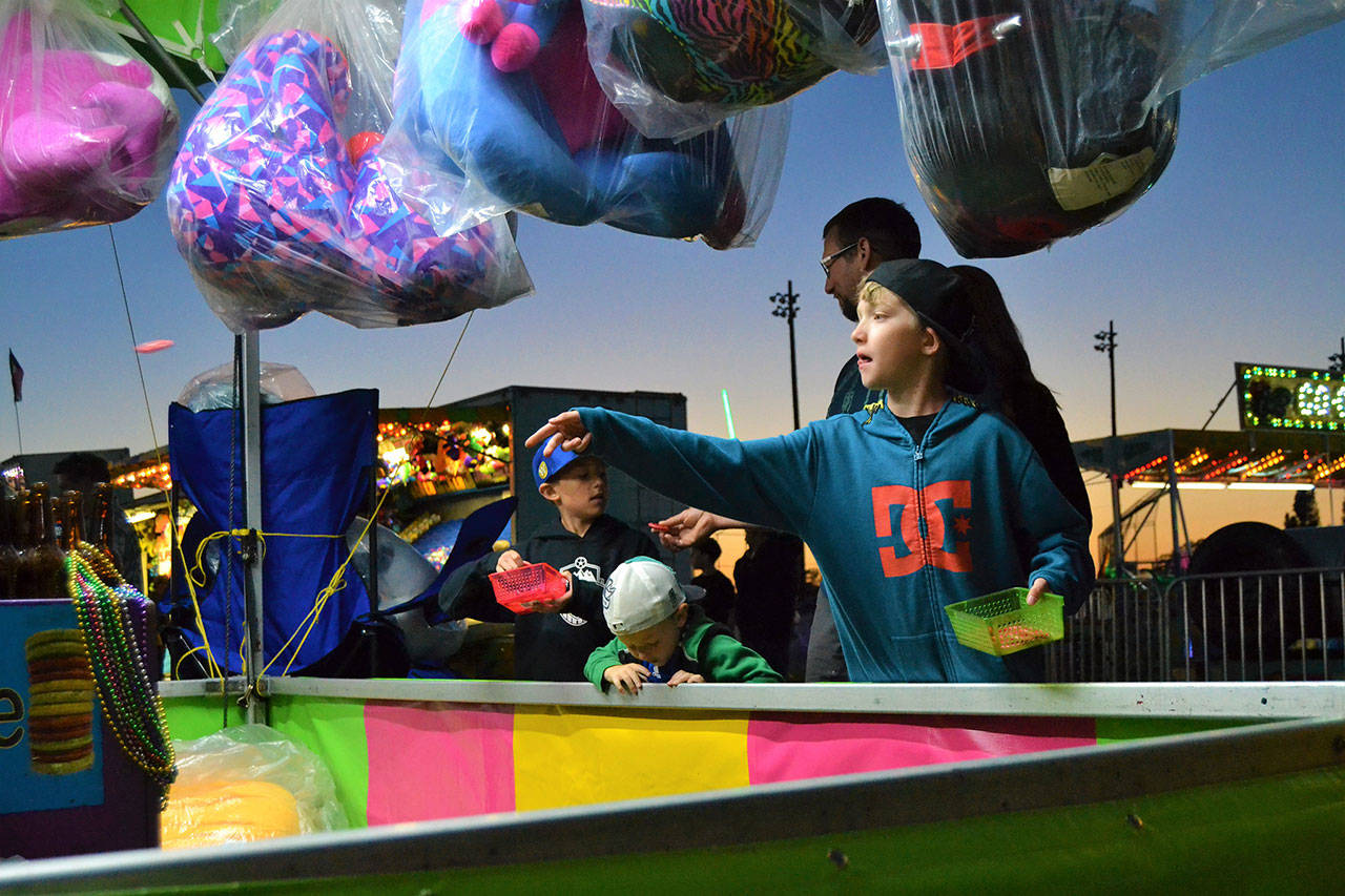 Blake Bacchus makes a throw in the ring toss as his brothers Nolan and Roman wait their turn at the 2018 carnival of the Sequim Irrigation Festival. (Matthew Nash /Olympic Peninsula News Group)