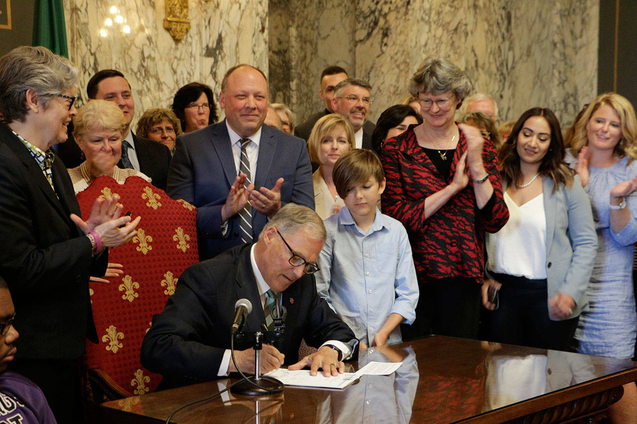 Gov. Jay Inslee signs a measure that puts the state on track to create the first public option health insurance in the country Monday in Olympia. (Rachel La Corte/The Associated Press)