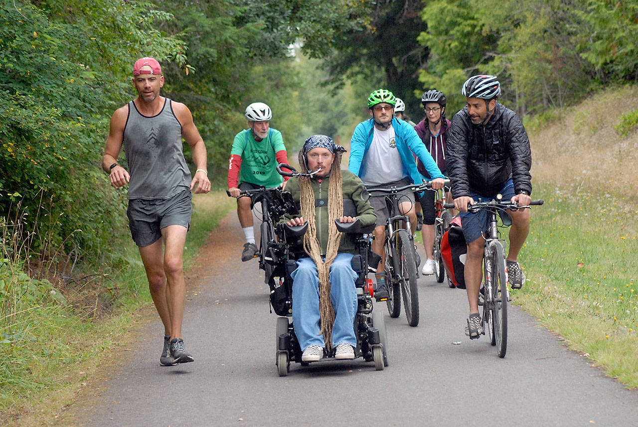 Ian Mackay of Agnew, center, leads a contingent of friends and supporters on bicycles and on foot from his motorized wheelchair along the Olympic Discovery Trail near 18th Street in Port Angeles during Saturday’s segment of the three-day Sea to Sound group ride across a portion of the North Olympic Peninsula. (Keith Thorpe/Peninsula Daily News)