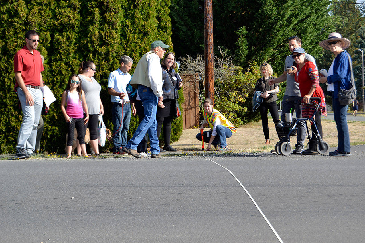 Katie Cole, Sequim associate engineer, measures a roadway as residents and consultants look on during a walking tour for the South Sequim Complete Streets project. Some residents on the tour said downtown neighborhoods are too small for new amenities and increased traffic. (Matthew Nash/Olympic Peninula News Group)