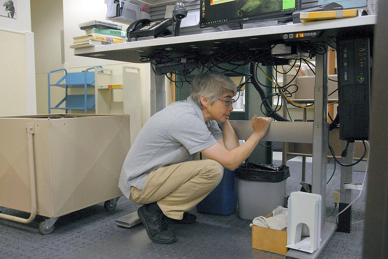 Jan Stark, a customer service representative for the North Olympic Library System, ducks under a desk at the Port Angeles Library during Thursday’s Great Washington ShakeOut. (Keith Thorpe/Peninsula Daily News)