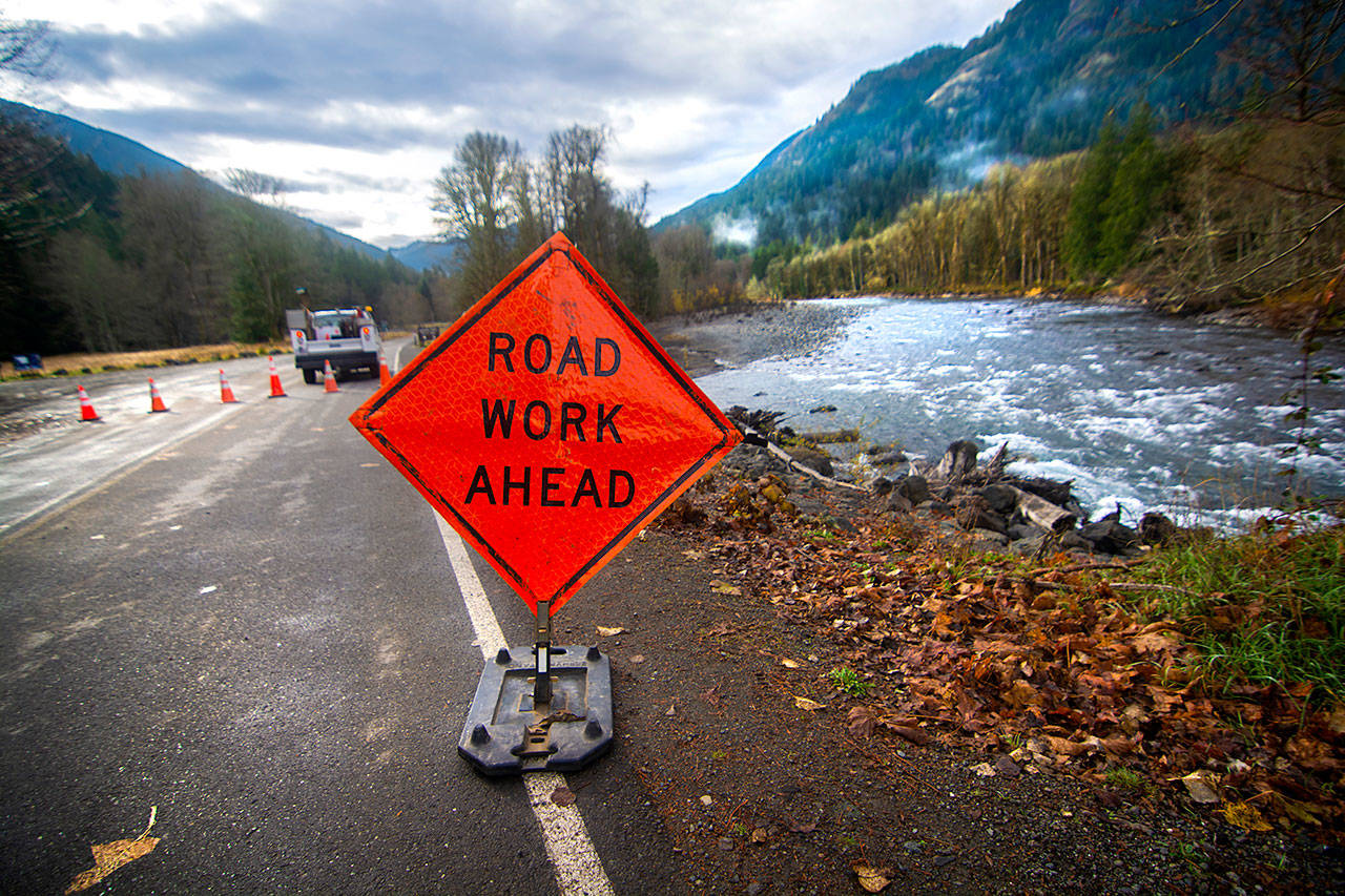 The Elwha River flows past a sign that says “road work ahead” Thursday as crews move rocks to prevent people from driving on the field at the entrance to Olympic National Park. Access to the Elwha Valley will be limited during reconstruction of Olympic Hot Springs Road. (Jesse Major/Peninsula Daily News)