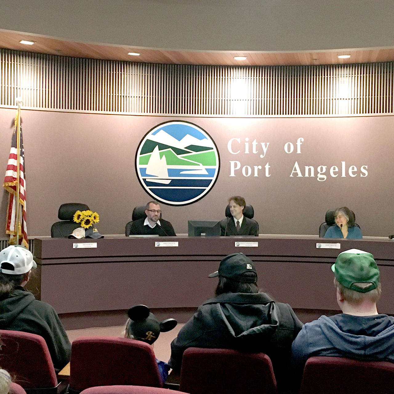 Sunflowers were placed near Jim Moran’s former seat on the Port Angeles City Council dais Tuesday. Moran, 71, died in his sleep late Friday or early Saturday. Council members Mike French, left, Lindsey Schromen-Wawrin and Mayor Sissi Bruch are shown reflecting on their former colleague. (Rob Ollikainen/Peninsula Daily News)