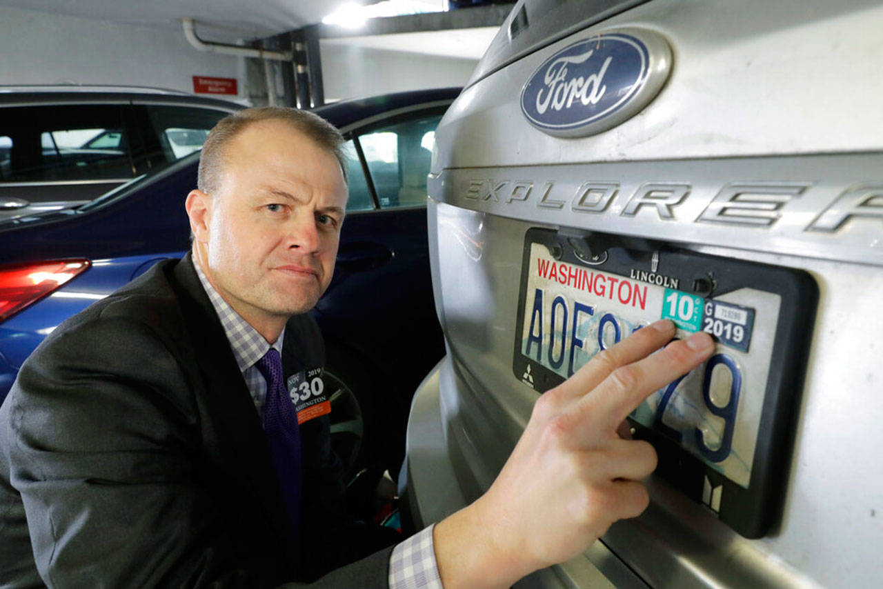 Tim Eyman, a career anti-tax initiative promoter, poses for a photo with the expired car registration tabs on his SUV on Tuesday, Nov. 26, 2019, in a parking garage in Seattle, following a hearing in King County Superior Court where lawyers for cities and counties across Washington state asked King County Judge Marshall Ferguson to block Eyman’s $30 I-976 car tab measure, which was approved by voters in the last election, saying it was misleading and violates Washington’s Constitution. Eyman says that until the issue is resolved and the state implements the lower car tab fees outlined in the measure, he is refusing to renew his tabs as a protest and is urging others not to do so as well. (AP Photo/Ted S. Warren)