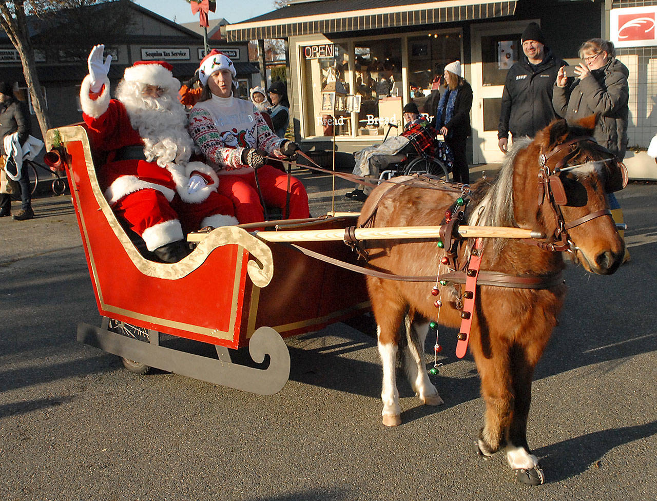 Santa Claus, portrayed by Joe Borden, accompanied by sleigh driver Molly Dickson and pulled by Minion, arrives at Centennial Place to kick of the Christmas season in Sequim on Saturday. The arrival was preceded by a concert of holiday music performed by the Sequim City Band. (Keith Thorpe/Peninsula Daily News)