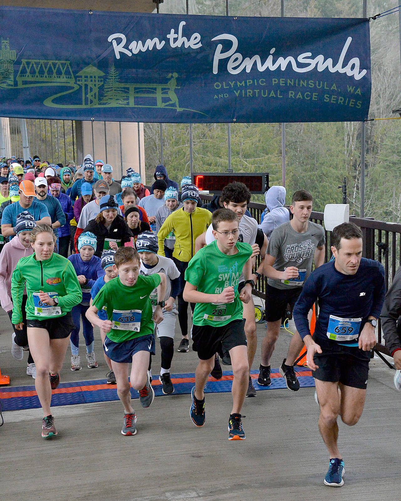 Runners cross the starting line during the Elwha Bridge 5K/10K Run, the first race in the second annual Run the Peninsula series. Women’s 10K winner Lauren Larson of Port Angeles is at far left, while male 5K winner Colby Ellefson and male 10K winner John Mauro of Port Townsend are at right. (EnMotive Photography)