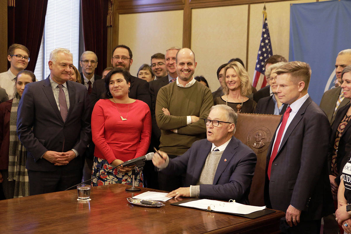 Washington Gov. Jay Inslee, seated, gestures after he signed a measure that changes the structure of a new business and occupation tax surcharge levied on some professional services and technology companies in order to create a more stable revenue stream for the state’s college grant program, Monday, Feb. 10, 2020, in Olympia. The program guarantees aid to college students at or below the state’s median family income, based on a sliding scale that increases the grant as family income drops. (Rachel La Corte/The Associated Press)