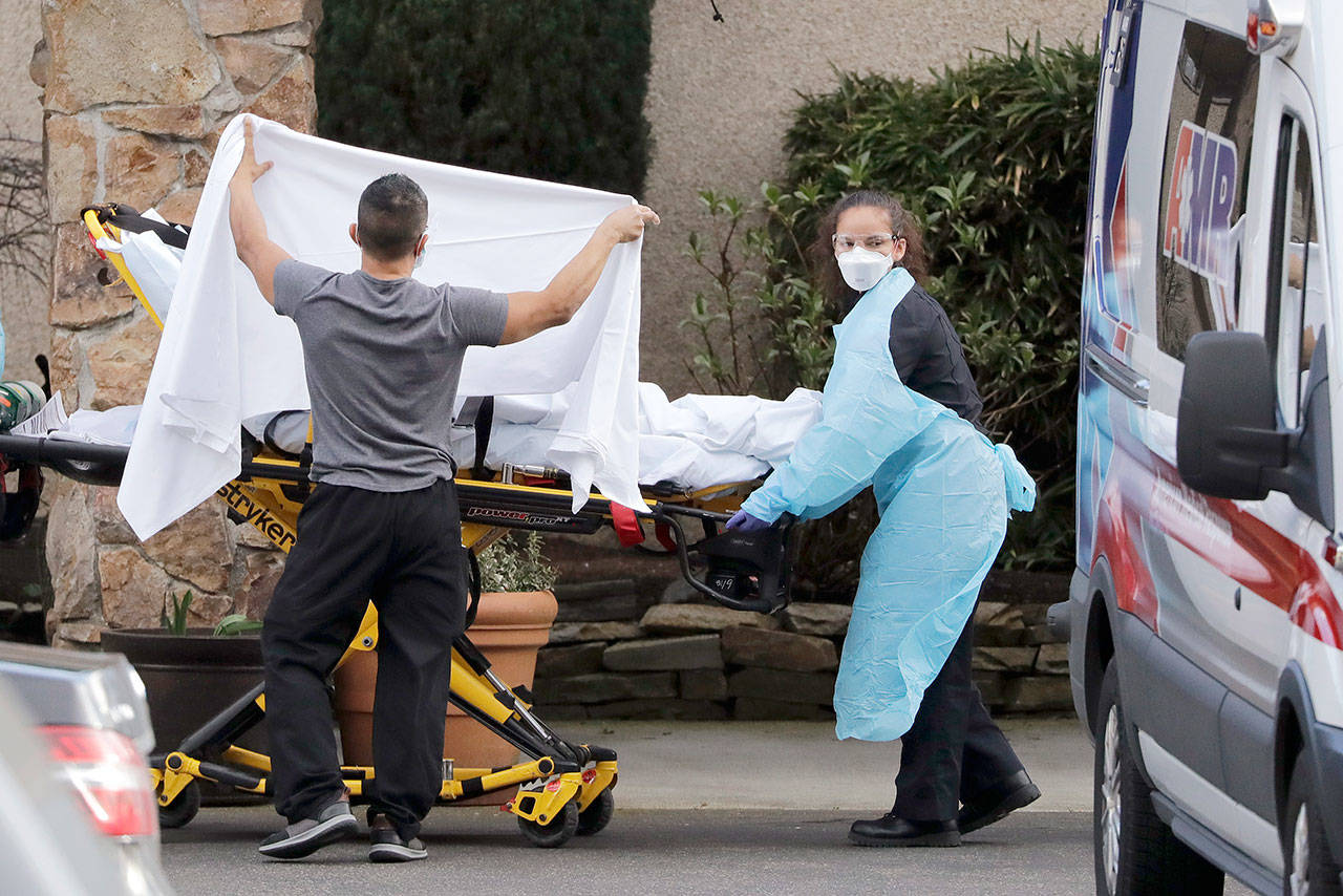 A staff member blocks the view as a person is taken by a stretcher to a waiting ambulance from a nursing facility where more than 50 people are sick and being tested for the COVID-19 virus, Saturday, Feb. 29, 2020, in Kirkland. Health officials reported two cases of COVID-19 virus connected to the Life Care Center of Kirkland. One is a Life Care worker, a woman in her 40s who is in satisfactory condition at a hospital, and the other is a woman in her 70s and a resident at Life Care who is hospitalized in serious condition. Neither have traveled out of the country. (Elaine Thompson/The Associated Press)