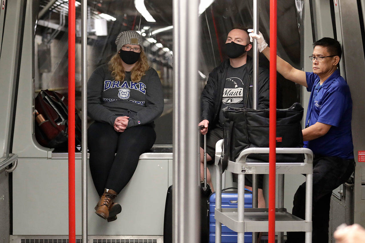 Travelers Meredith Ponder, left, and Coleby Hanisch, both of Des Moines, Iowa, wear masks to remind them not to touch their faces as they ride a train at Seattle-Tacoma International Airport Tuesday, March 3, 2020, in SeaTac. Six of the 18 Western Washington residents with the coronavirus have died as health officials rush to test more suspected cases and communities brace for spread of the disease. All confirmed cases of the virus in Washington are in Snohomish and King counties. (Elaine Thompson/The Associated Press)