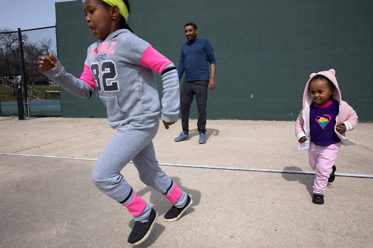 Aragaw Beyene, center, of Washington, plays with his cousins’ children, Eldana Tilahune, 6, left, and Meklit Tilahune, 2, on Monday, March 16, 2020, at a public park in northwest Washington. Beyene and his extended family are taking turns watching each other’s children so the others can work while schools are closed due to coronavirus precautions. “I normally drive an Uber,” says Beyene, “but it’s scary to drive an Uber right now with the coronavirus. I haven’t gone to work since Friday. Although I hear there is not much work.” The family says they may stop taking the children to parks outside due to coronavirus fears. (Jacquelyn Martin/The Associated Press)