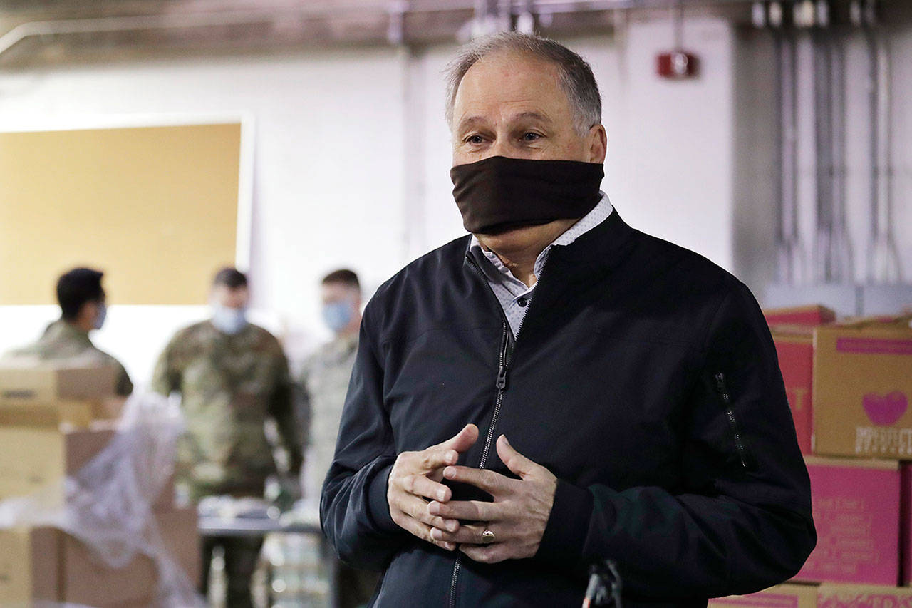 Gov. Jay Inslee wears a makeshift mask as he speaks with media members while visiting inside Nourish Pierce County warehouse Friday, in Lakewood. (Elaine Thompson/The Associated Press)