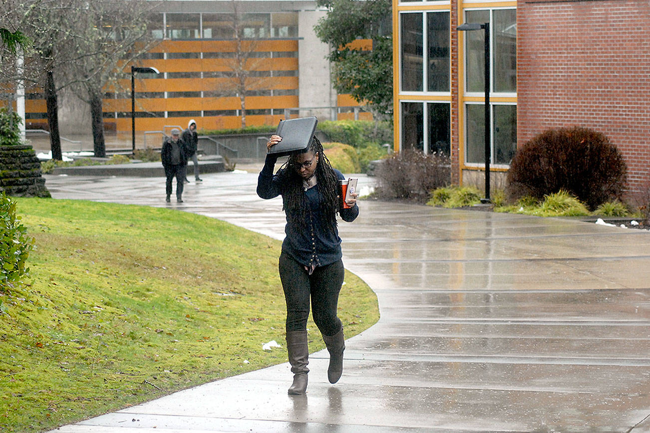 Nitasha Lewis, a manager with the Upward Bound program at Peninsula College, uses a paper valise to keep her head dry as she walks across the college’s Port Angeles campus Feb. 6, 2020. The college is going to online classes for the entirety of the 2020 spring quarter. (Keith Thorpe/Peninsula Daily News file)