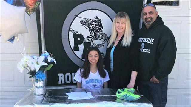 Port Angeles Roughrider Kynzie DeLeon, left, signs her letter of intent to run track and field and cross country at Warner Pacific University in Portland, Ore., along with her parents, Tamie and Dan DeLeon, at right.