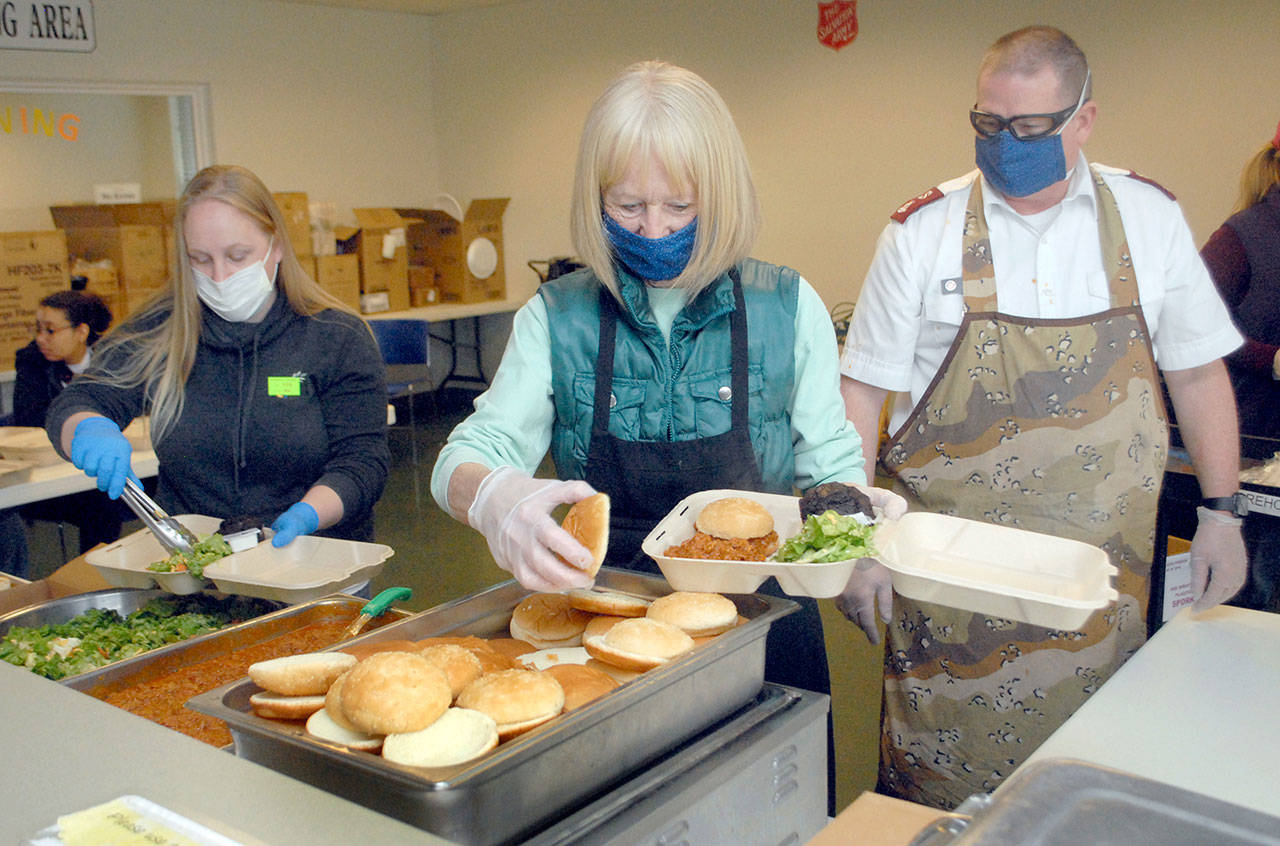 Volunteers, from left, Michelle Warren of Port Angeles and Phyllis Meyter of Sequim, prepare take-out meals as Major Ron Wehnau, right, stands by to deliver them to people waiting outside the Port Angeles Salvation Army’ kitchen for lunch on Friday. (Keith Thorpe/Peninsula Daily News)