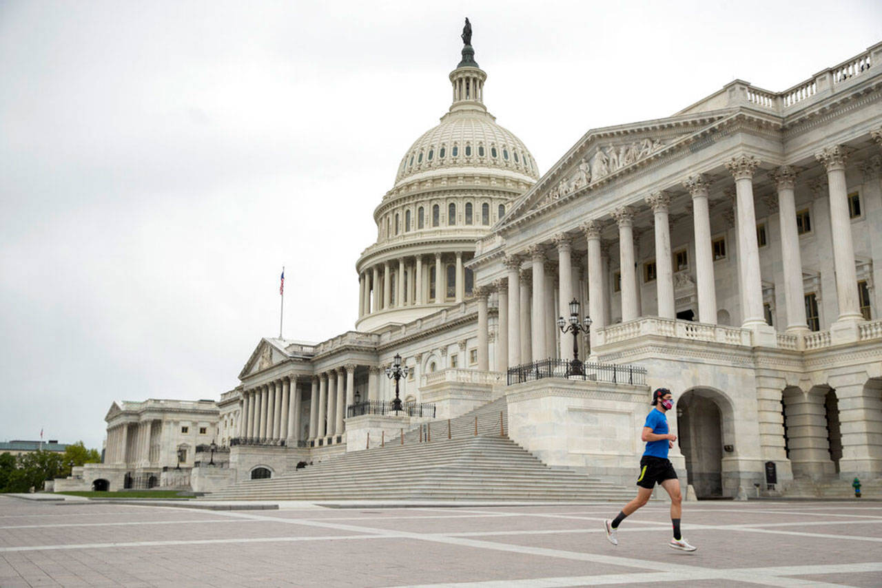 A man wearing a mask depicting American flags jogs past the U.S. Capitol Building on Tuesday, April 28, 2020, in Washington. The U.S. House of Representatives has canceled plans to return next week, a reversal after announcing it a day earlier. (Andrew Harnik/Associated Press)