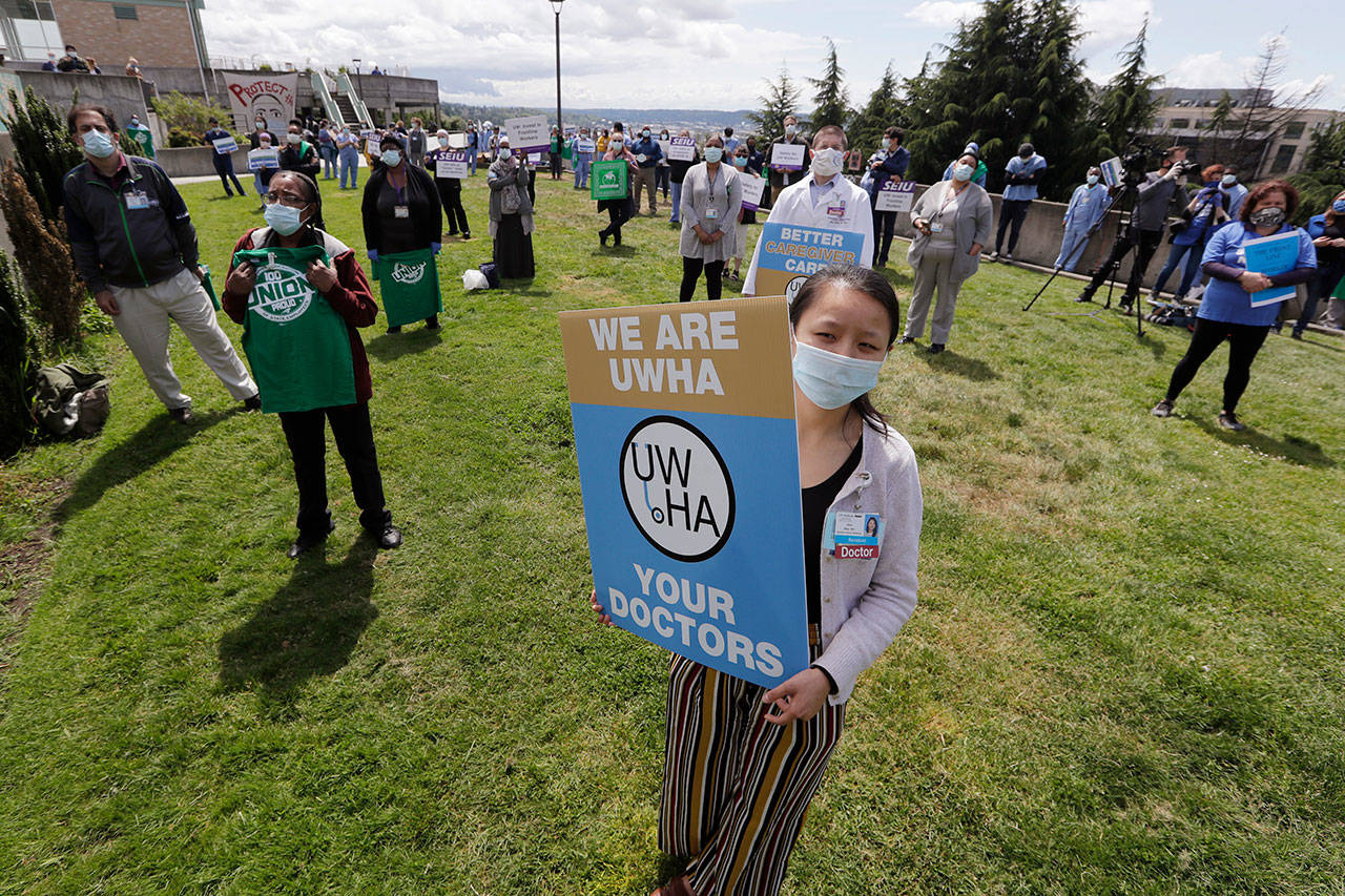 Health care workers stand some six feet apart at Harborview Medical Center, a part of UW Medicine, during a noon hour demonstration asking management to do more to protect staff, patients and the public amid the COVID-19 pandemic Thursday in Seattle. Protest organizers said UW Medicine has failed to fully implement public health guidance designed to flatten the curve, and has refused to extend agreements with unions that provide economic protections for employees. (Elaine Thompson/Associated Press)