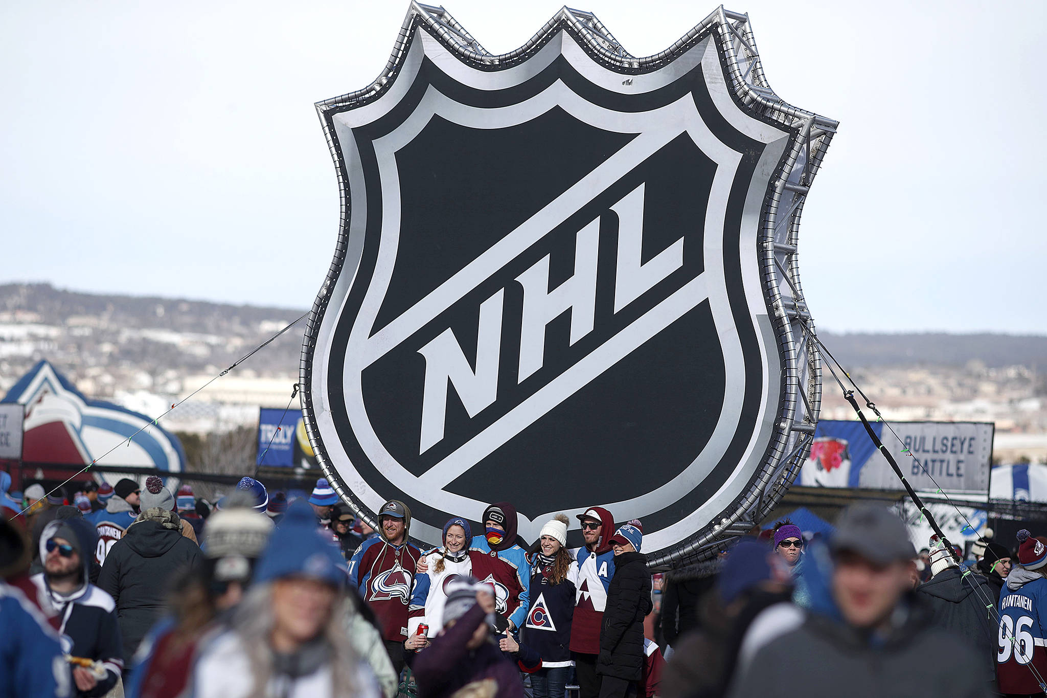 Fans pose below the NHL league logo at a display outside Falcon Stadium before an NHL Stadium Series outdoor hockey game between the Los Angeles Kings and Colorado Avalanche, at Air Force Academy, Colo., on Feb. 15, 2020. The NHL Players’ Association’s executive board is voting on a 24-team playoff proposal as the return-to-play format. (David Zalubowski/Associated Press file)