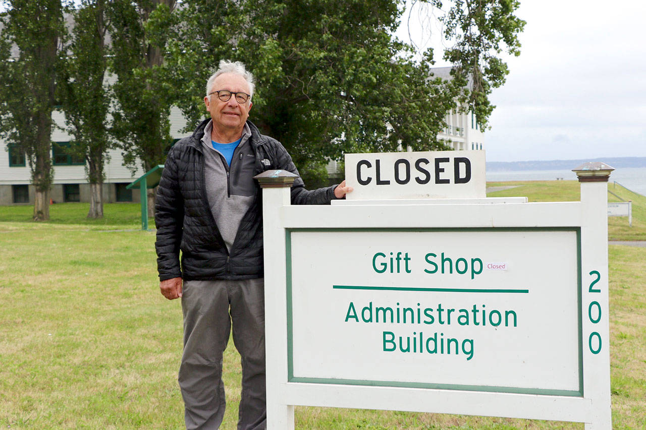 Friends of Fort Worden president Terry LeLievre stands with the sign proclaiming the Fort Worden State Park gift shop closed. The closure has cut into the group’s revenues and so it is pursuing other fundraising measures to help it support the park. (Ken Park/Peninsula Daily News)