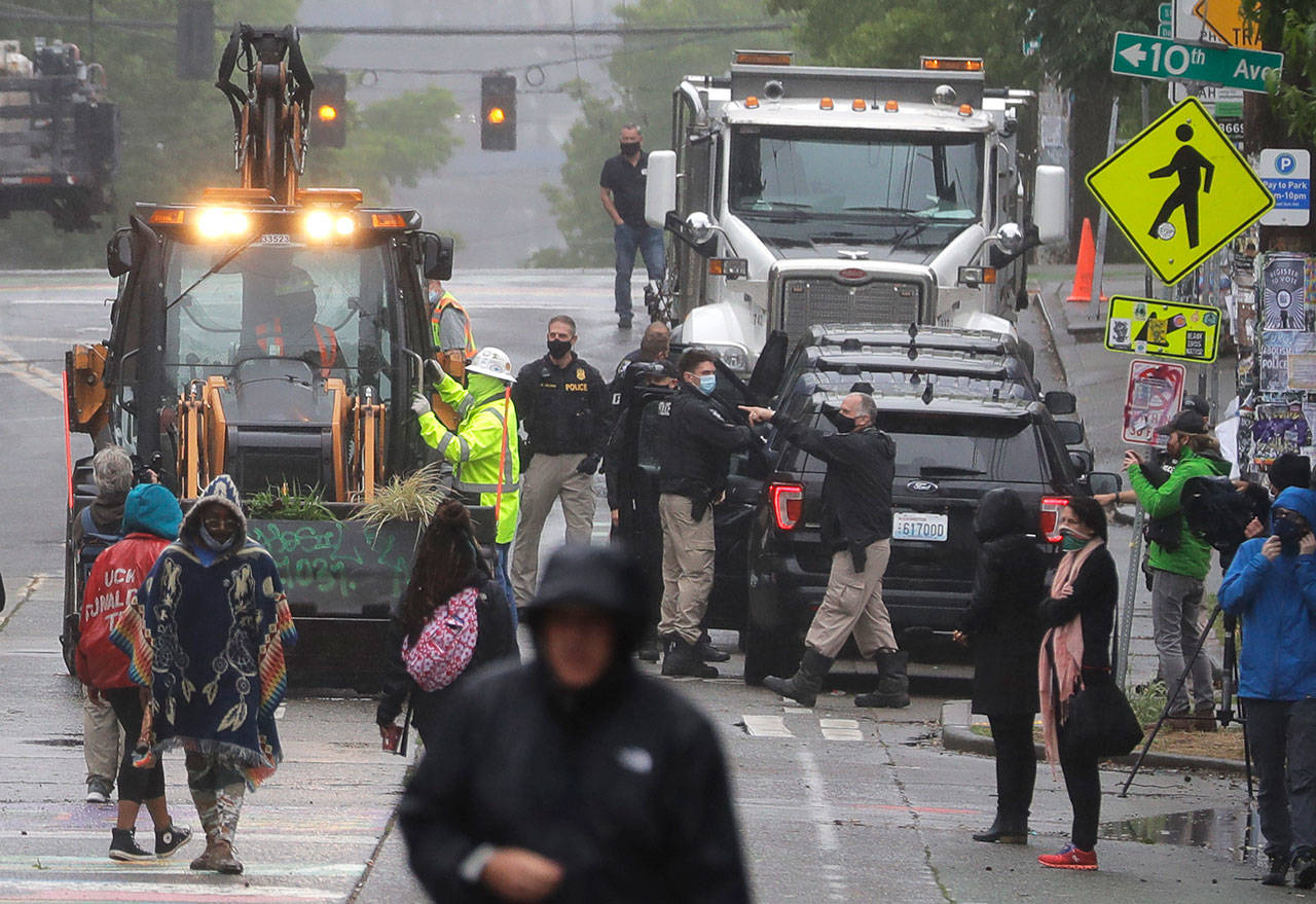 Seattle Police, at right, look on as Department of Transportation workers remove barricades at the intersection of 10th Ave. and Pine St., Tuesday, June 30, 2020 at the CHOP (Capitol Hill Occupied Protest) zone in Seattle. Protesters quickly moved couches, trash cans and other materials in to replace the cleared barricades. The area has been occupied by protesters since Seattle Police pulled back from their East Precinct building following violent clashes with demonstrators earlier in the month. (AP Photo/Ted S. Warren)