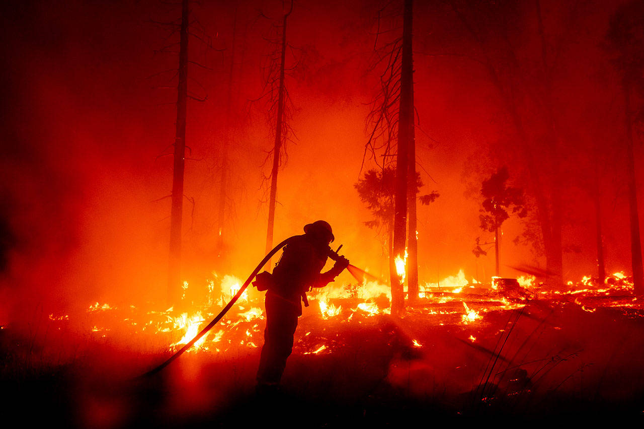 In this Sept. 7, 2020, file photo, a firefighter battles the Creek Fire as it threatens homes in the Cascadel Woods neighborhood of Madera County, Calif. This year’s fires have taxed the human, mechanical and financial resources of the nation’s wildfire fighting forces to a degree that few past blazes did. And half of the fire season is yet to come. (Noah Berger/Associated Press file)