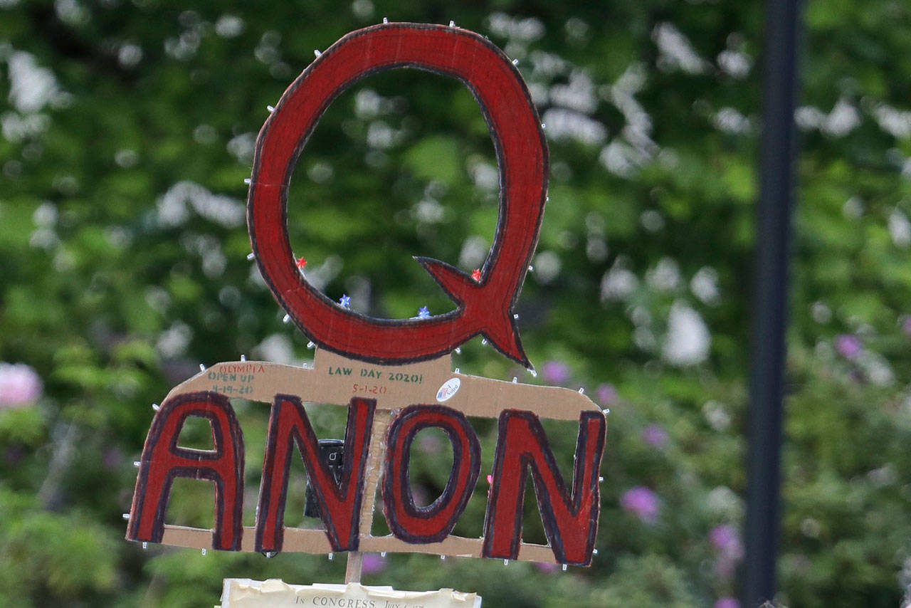 In this May 14, 2020, file photo, a person carries a sign supporting QAnon at a protest rally in Olympia, Wash. Facebook said Tuesday, Oct. 6, 2020, that it will remove Facebook pages, groups and Instagram accounts for “representing QAnon.” (AP Photo/Ted S. Warren/Associated Press file)