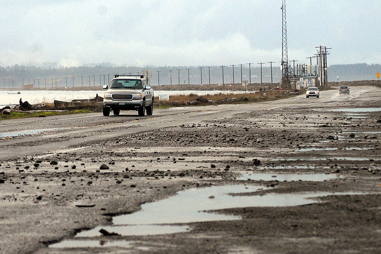 Vehicles make their away along a rock-strewn stretch of Ediz Hook Road in Port Angeles after high waves pushed debris across a parking area and a section of roadway. (Keith Thorpe/Peninsula Daily News)