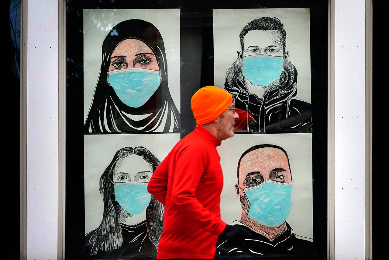 In this Nov. 16 photo, a runner passes by a window displaying portraits of people wearing face coverings to help prevent the spread of the coronavirus in Lewiston, Maine. (AP Photo/Robert F. Bukaty)