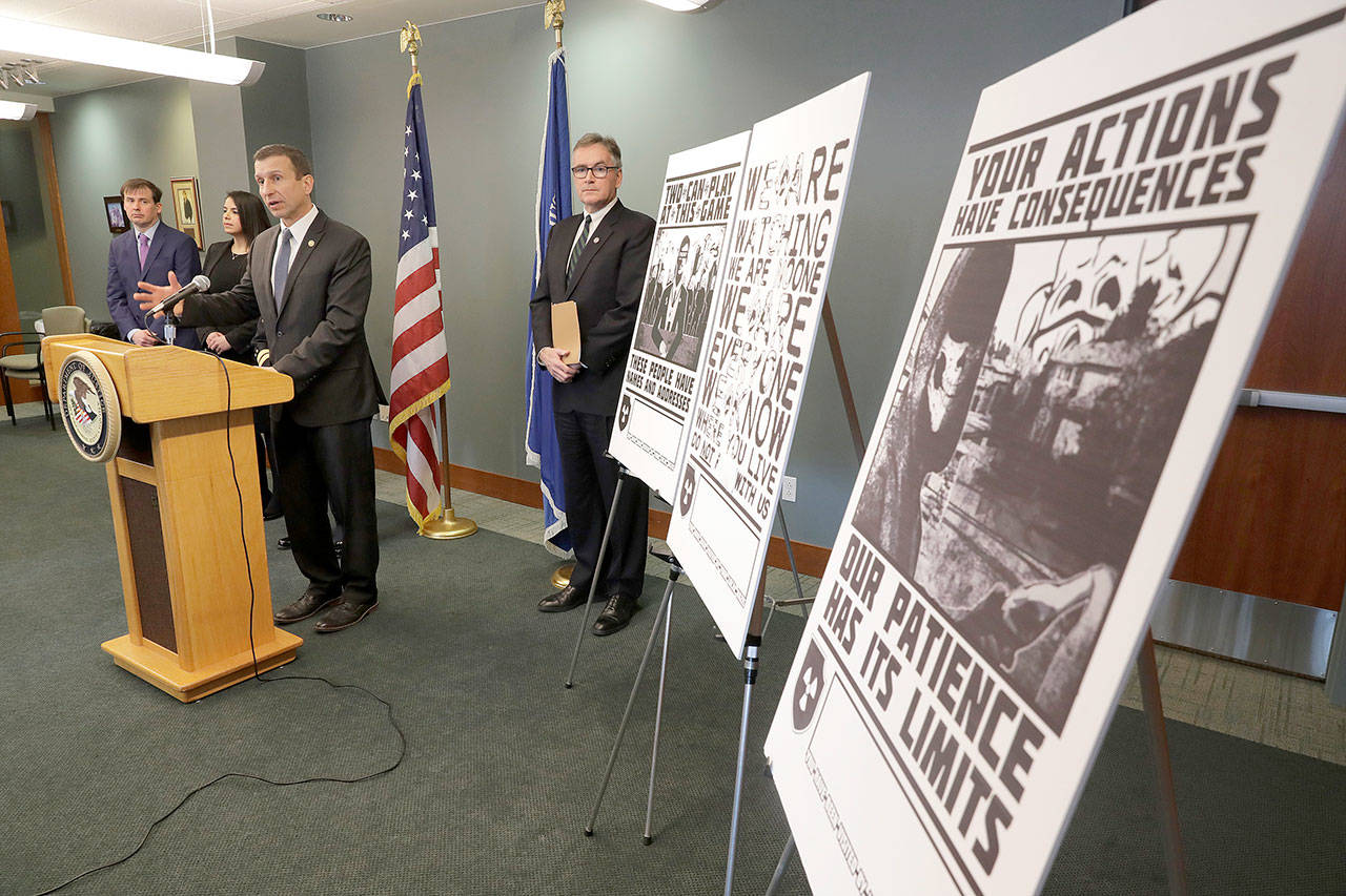 In this Feb. 26, 2020, file photo, Raymond Duda, FBI Special Agent in Charge in Seattle, speaks during a news conference at a podium, about charges against a group of alleged members of the neo-Nazi group Atomwaffen Division for cyber-stalking and mailing threatening communications, including the Swastika-laden posters at right, in a campaign against journalists in several cities. Johnny Roman Garza, an Arizona man has been sentenced to 16 months in prison for his role in a neo-Nazi group’s coordinated campaign to threaten and harass journalists, activists and other targets on both U.S. coasts Wednesday, Dec. 9, 2020. (Ted S. Warren/Associated Press file)