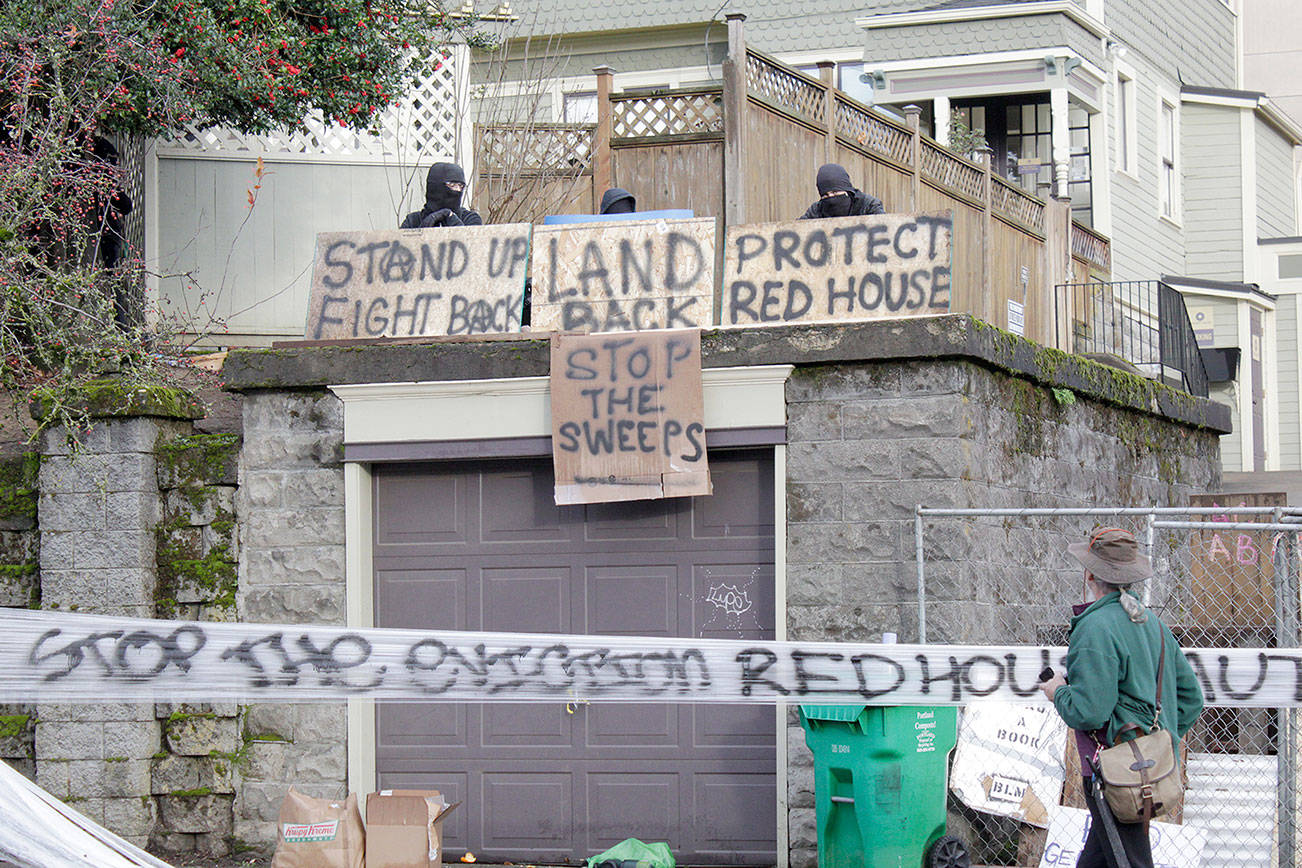 Masked protesters by an occupied home speak with a neighborhood resident opposed to their encampment and demonstration in Portland, Ore., on Wednesday, Dec. 9, 2020. Makeshift barricades erected by protesters are still up in Oregon's largest city a day after Portland police arrested about a dozen people in a clash over gentrification and the eviction of a family from a home. (AP Photo/Gillian Flaccus)