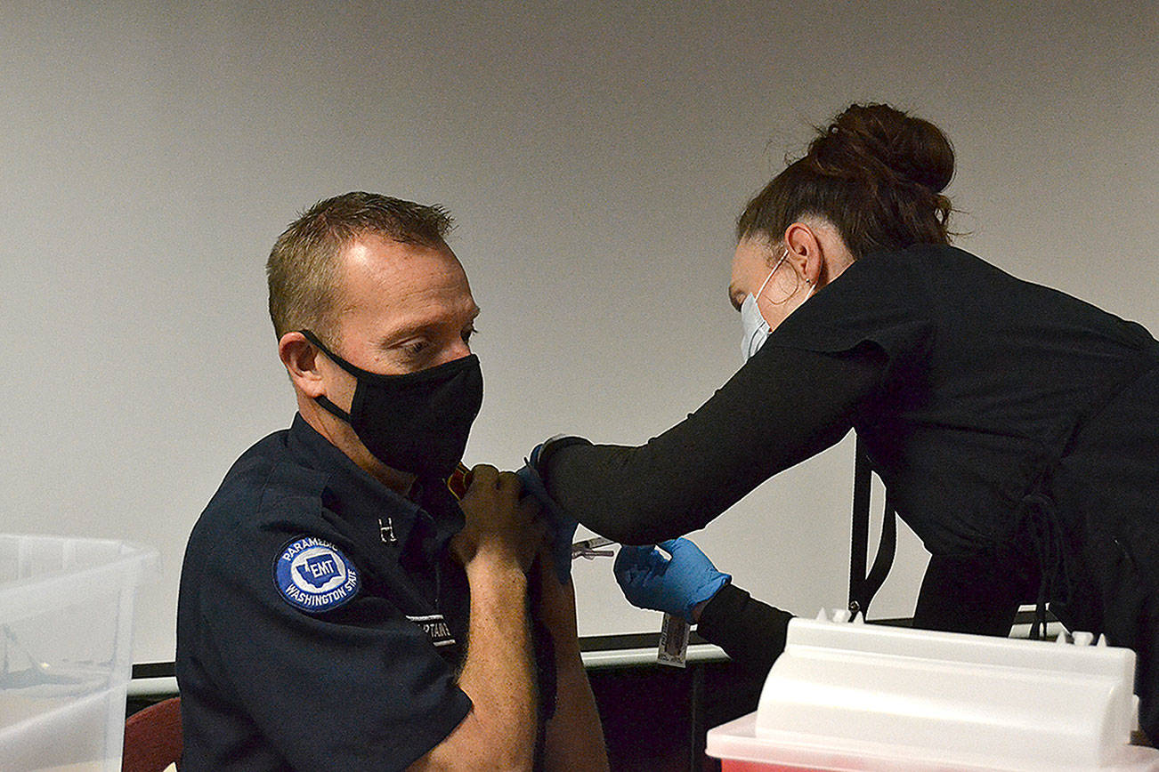 Nurse Kelly Bower with the Jamestown Family Health Clinic gives a Moderna COVID-19 Vaccine to Capt. Derrell Sharp with Clallam County Fire District 3 on Tuesday at the fire station’s headquarters. Clinic leaders say they’ve begun circulating the vaccine to first responders and plan to offer community vaccinations in the coming weeks. (Matthew Nash/Olympic Peninsula News Group)