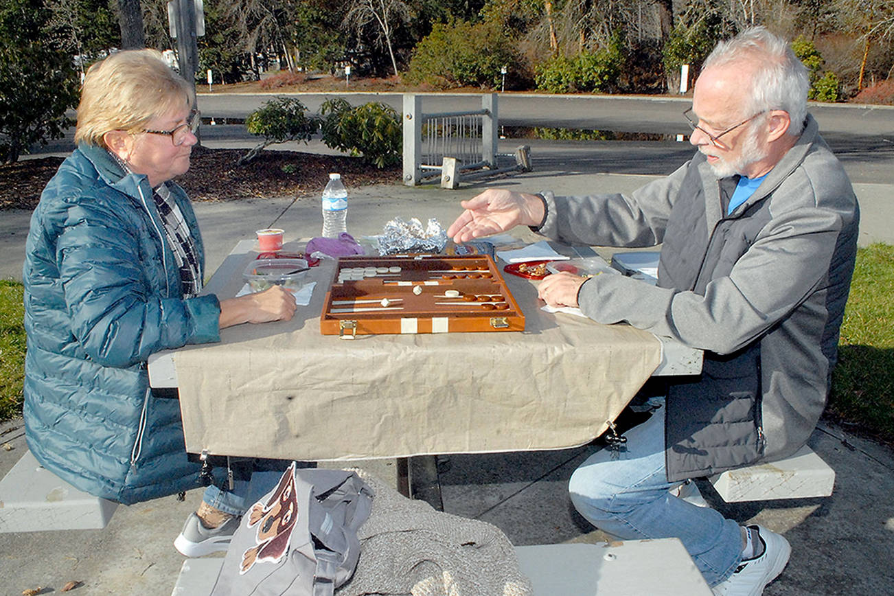 Susie and Larry Ormbrek of Sequim enjoy a sunny Tuesday to play a game of backgammon while eating lunch near the shore of Sequim Bay at John Wayne Marine in Sequim. The pair said they often try to take advantage of nice weather for outdoor dining. (Keith Thorpe/Peninsula Daily News)