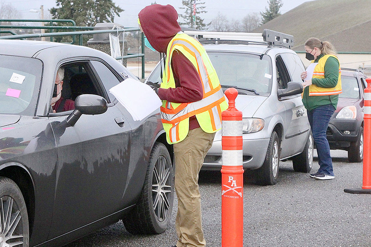 Volunteers Anthony Brigandi and Jennifer Rogers check out the next cars in line for their appointment to get a COVID-19 Pfizer vaccine Saturday morning at the Port Angeles High School campus. The whole process at the PAHS auxiliary gym and adjacent parking lot is run smoothly by over 60 volunteers from across the county and takes about 30 minutes. (Dave Logan/For Peninsula Daily News)