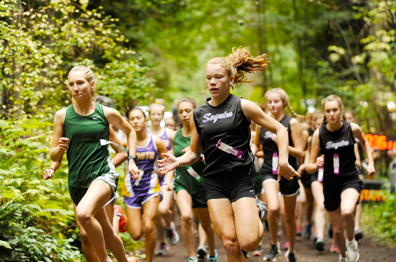 Port Angeles’ Lauren Larson, left, and Sequim’s Riley Pyeatt lead the pack at the beginning of a 2019 cross country race at Robin Hill Park. Prep runners can now run without masks at competitions after a change in state guidance. (Michael Dashiell/Olympic Peninsula News Group)