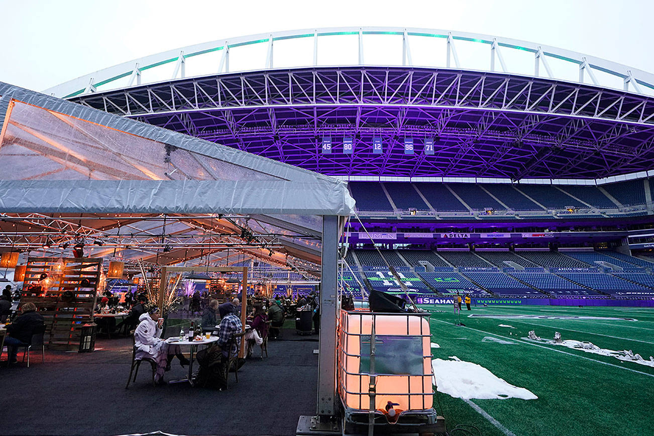 People eat dinner in an outdoor dining tent set up at Lumen Field, the home of the Seattle Seahawks NFL football team, Thursday, Feb. 18, 2021, in Seattle. The "Field To Table" event was the first night of several weeks of dates that offer four-course meals cooked by local chefs and served on the field at tables socially distanced as a precaution against the COVID-19 pandemic, which has severely limited options for dining out at restaurants in the area. (AP Photo/Ted S. Warren)