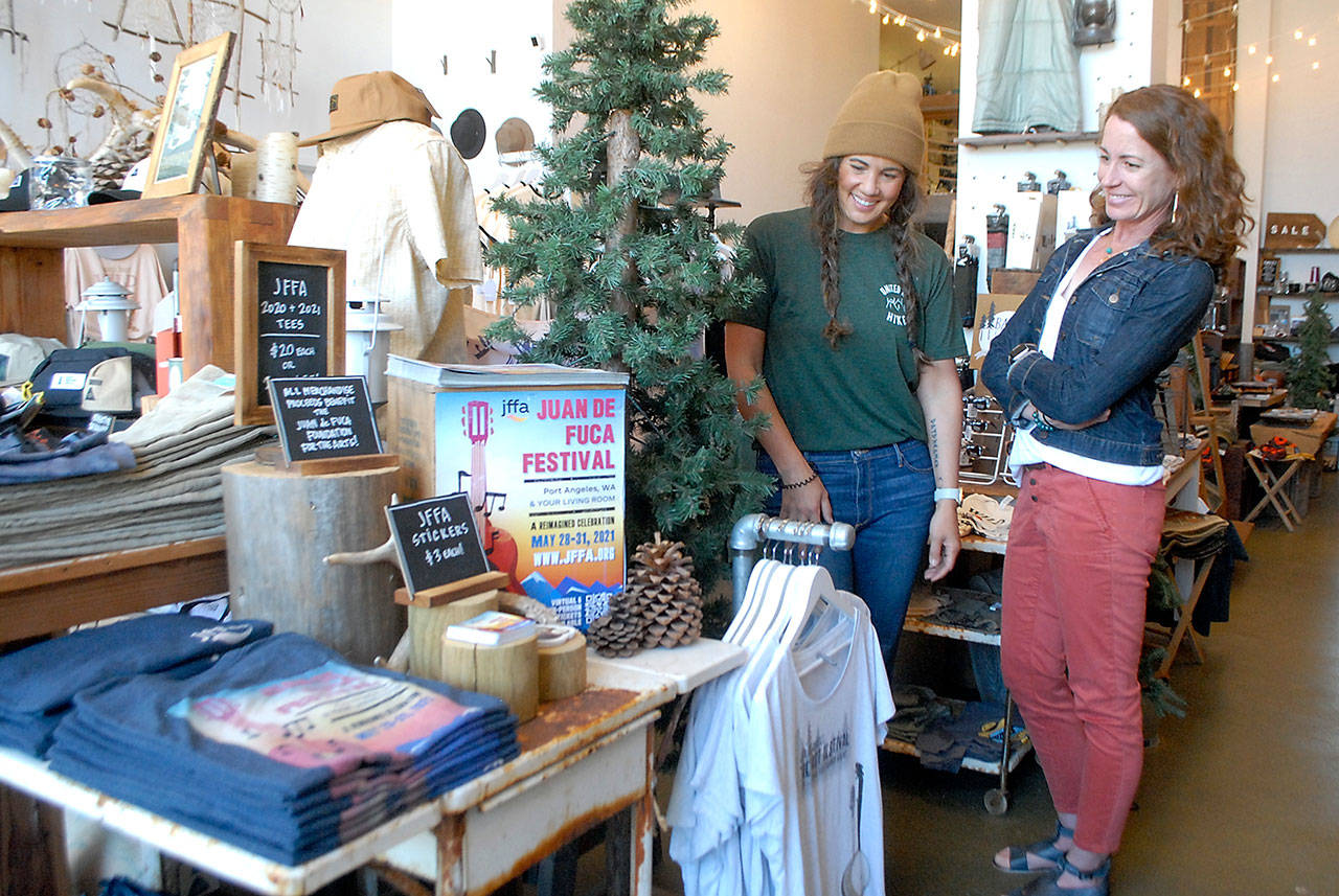 Hayley Sharpe, owner of MOSS, left, talks with Kayla Oakes, executive director of the Juan de Fuca Festival of the Arts, on Tuesday next to a display of festival merchandise offered at the downtown Port Angeles shop. The festival’s concerts and street fair return to the Vern Burton Community Center this Friday through Sunday. (Keith Thorpe/Peninsula Daily News)