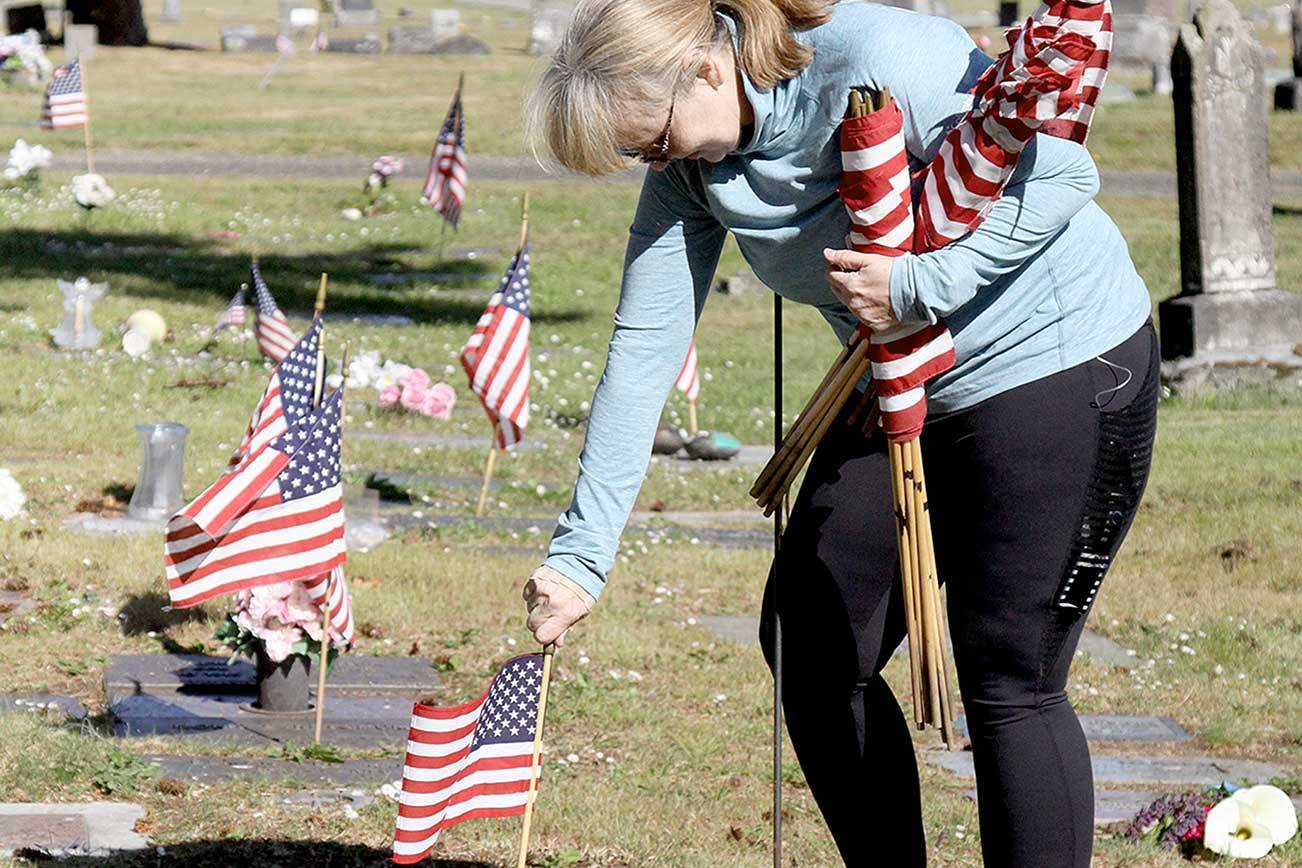 American Legion member Patricia Radford uses a sharp tool to poke a hole in the ground and then places an American flag near the grave of a service member. In preparation for Memorial Day, volunteers went to Ocean View Cemetery to place small flags on all the graves of former service members they could locate. They placed hundreds of flags Saturday morning to honor and remember those who gave their service to the country. (Dave Logan/for Peninsula Daily News)