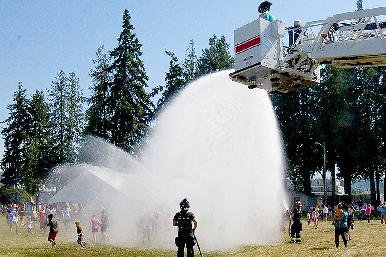 Firefighters from the Port Angeles Fire Department spray between 150 and 200 people from a ladder and two other hoses on Monday afternoon at Erickson Playfield. The community event was scheduled as temperatures soared to 97 degrees. (Dave Logan/For Peninsula Daily News)