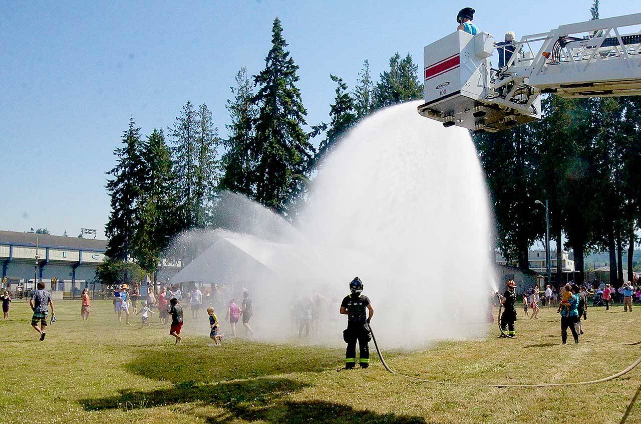 Firefighters from the Port Angeles Fire Department spray between 150 and 200 people from a ladder and two other hoses on Monday afternoon at Erickson Playfield. The community event was scheduled as temperatures soared to 97 degrees. (Dave Logan/For Peninsula Daily News)