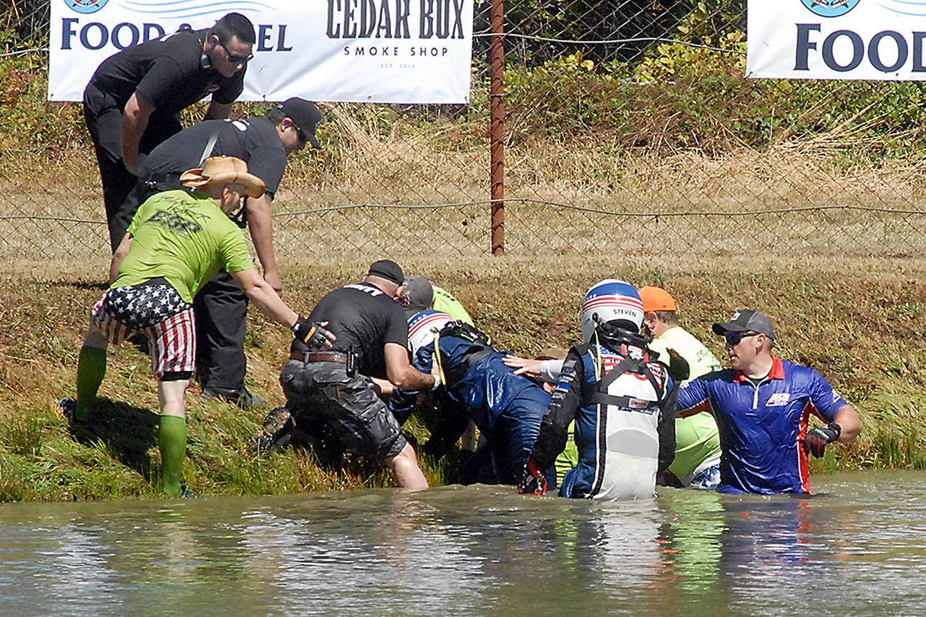 Keith Thorpe/Peninsula Daily News
Extreme Sports Park personnel and emergency medical workers assist navigator Lisa Bowman, left, and driver Steven Church of the Ron Domoe Racing crew after their Bad Influence sprint boat was catapulted over an embankment into the track's spin-out pool and immediately sank, leaving both briefly trapped under water during a qualifying race on Saturday in Port Angeles. For results, see Sports on Monday.