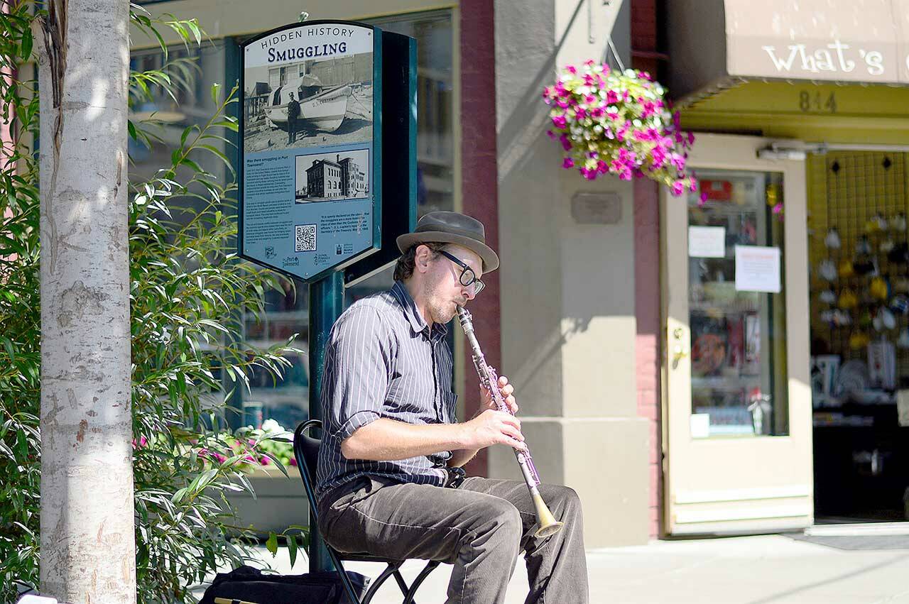 Busker Jonathan Doyle plays on Water Street in Port Townsend beside the Hidden History sign about smuggling during the 19th and 20th centuries. The series of Hidden History panels inspire twice-monthly walking tours around downtown. (Diane Urbani de la Paz/Peninsula Daily News)