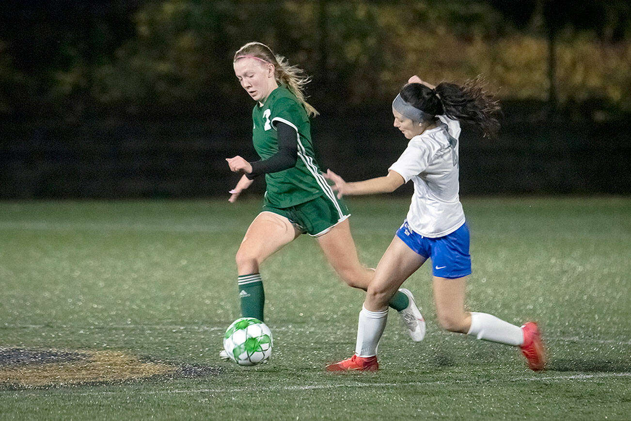 Jesse Major/for Peninsula Daily News
Port Angeles sophomore Izzy Felton dribbles by Olympic's Autumn Clark during the Roughriders 4-0 Bi-District win over the Trojans at Peninsula College's Wally Sigmar Field on Thursday