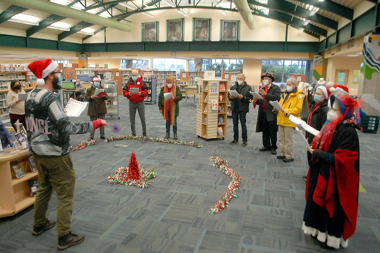 Keith Thorpe/Peninsula Daily News
Noah Smith, director of music ministry at Holy Trinity Lutheran Church, with hat at left, directs a collection of carolers from the church during a performance of holiday songs at the Port Angeles Public Library on Saturday. The church plans to hold virtual and in-person candlelight services on Christmas Eve. For more information, visit www.go2trinity.org.