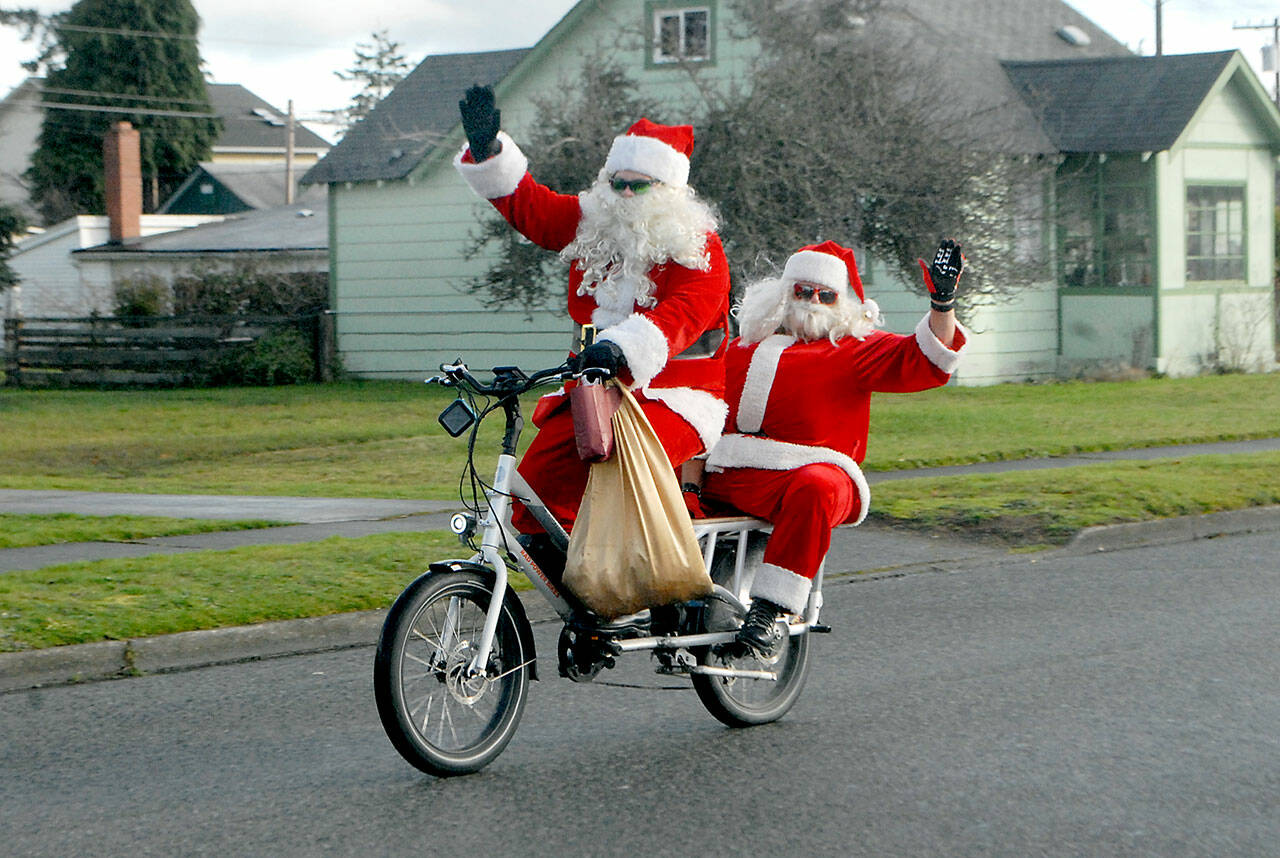 Jake Thornburg, front, and Chig Martin, both of Port Angeles, take on the Santa persona as they ride a motorized bicycle on West Third Street in Port Angeles on Christmas Eve. (Keith Thorpe/Peninsula Daily News)