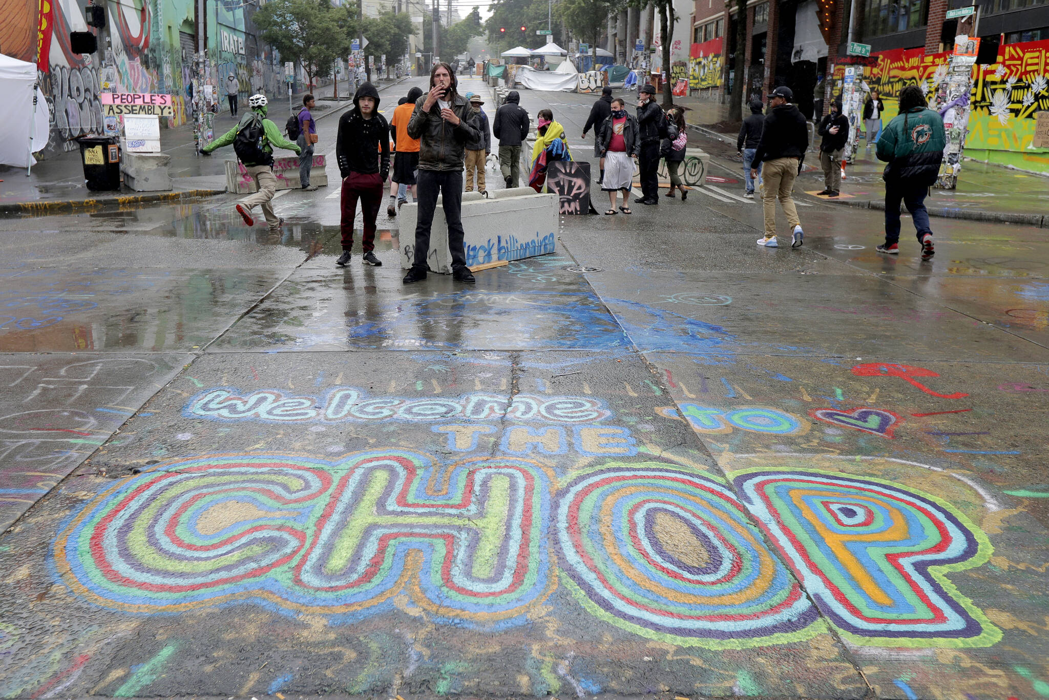 FILE - A sign on the street reads "Welcome to the CHOP" as protesters stand near barricades at the CHOP (Capitol Hill Occupied Protest) zone in Seattle on Tuesday, June 30, 2020. An investigation by the city's police watchdog shows Seattle Police exchanged detailed fake radio transmissions about a nonexistent group of menacing right-wing extremists at a crucial moment during 2020 racial justice protests. Officials said fabricating the group of Proud Boys violated department policies. (AP Photo/Ted S. Warren, File)