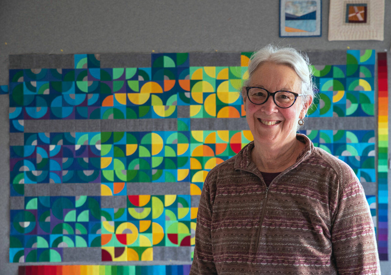 Fiber Artist Marla Varner stands in front of her temperature quilt. Each square is color coded to the high and low temperatures of each day of 2021 in her neighborhood in Sequim, with the smallest quarter circles signifying precipitation. (Emily Matthiessen/Olympic Peninsula News Group)