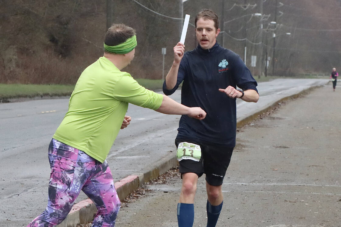 Chris Hartman passes the slap bracelet “baton” off to Jack Waknitz of the Sub Alpine Tees Racing Team at the Frosty Moss checkpoint next to the Boat Haven on the Port Angeles waterfront Saturday. (Dave Logan/for Peninsula Daily News)