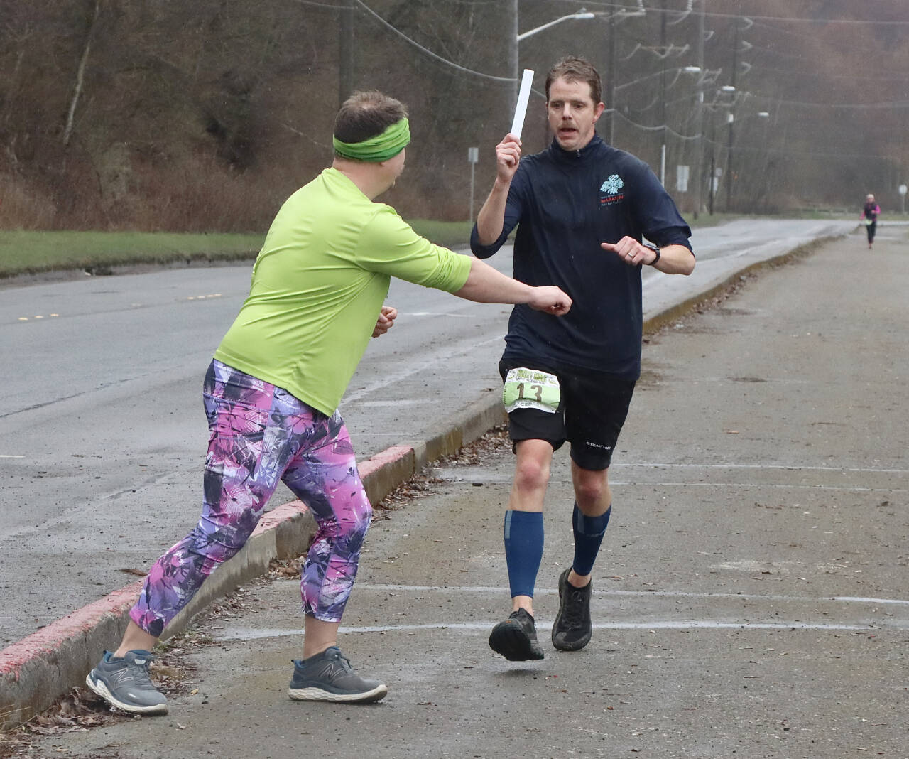 Chris Hartman passes the slap bracelet “baton” off to Jack Waknitz of the Sub Alpine Tees Racing Team at the Frosty Moss checkpoint next to the Boat Haven on the Port Angeles waterfront Saturday. (Dave Logan/for Peninsula Daily News)